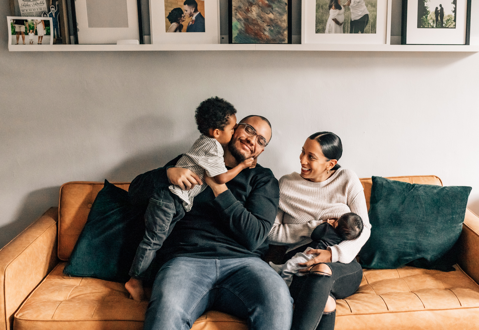 During their lifestyle newborn photo session a family of four laughs on their couch.