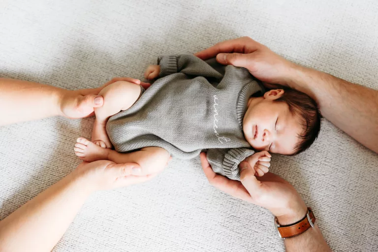 A sleeping baby is surrounded by his parents hands during newborn photos in Edmond, OK.