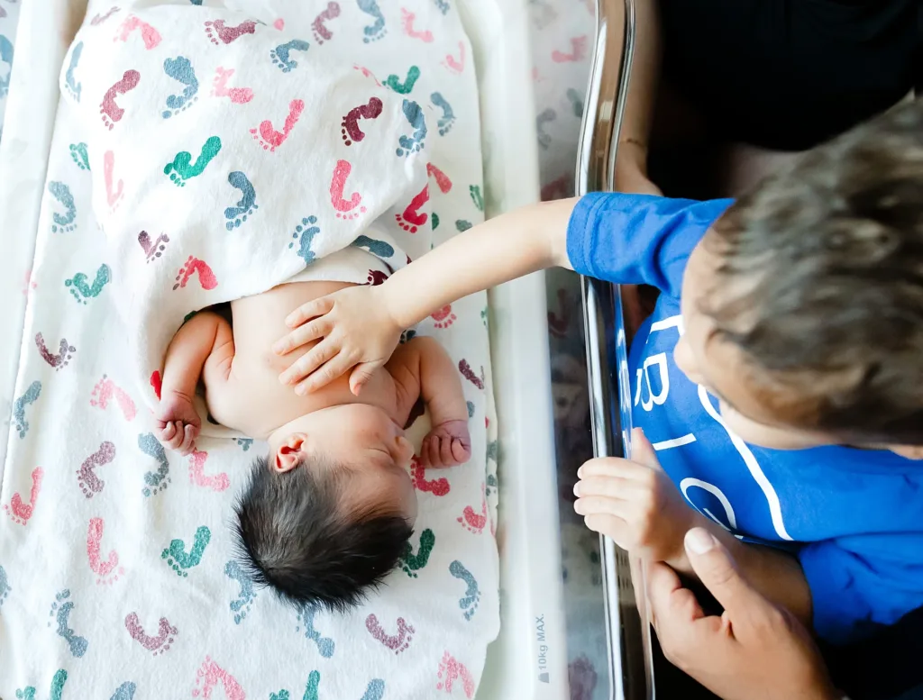 Big Brother looks at newborn baby in hospital crib during a fresh 48 session in OKC.