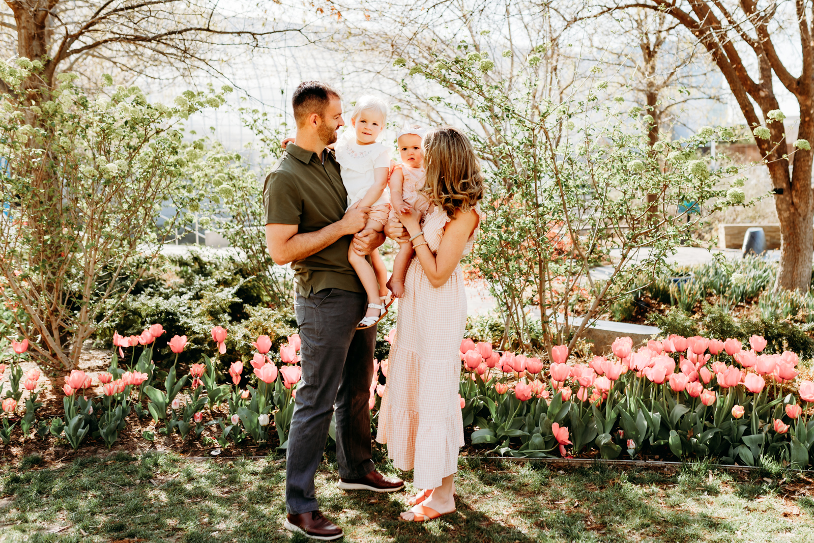 Parents stand with their toddler girls in the tulips at OKC Myriad Botanical Gardens during a family photo session.