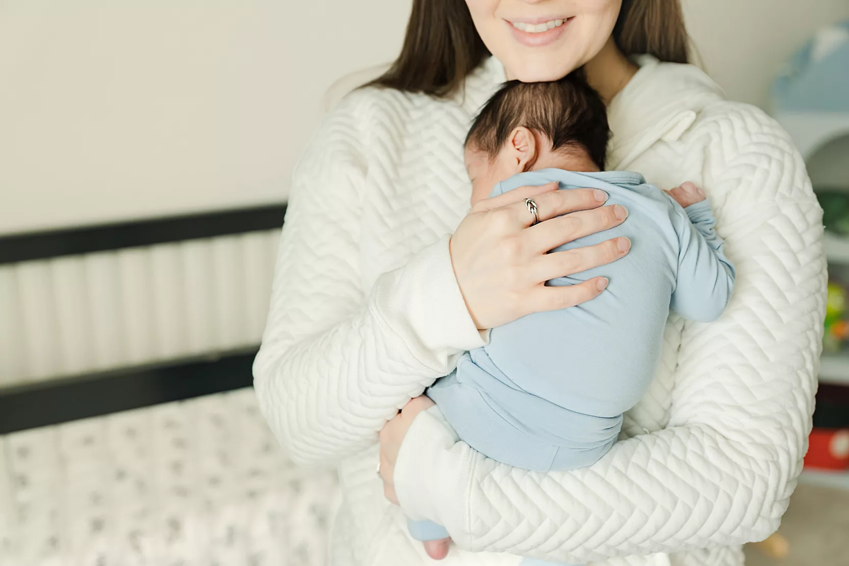 Baby in blue snuggled in mama's arms at home.