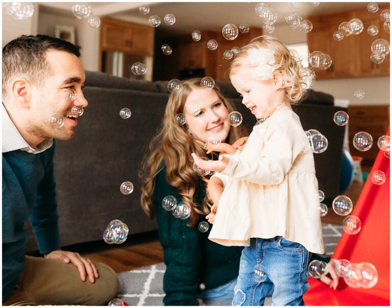 Mom, dad and daughter in yellow shirt play with bubbles.