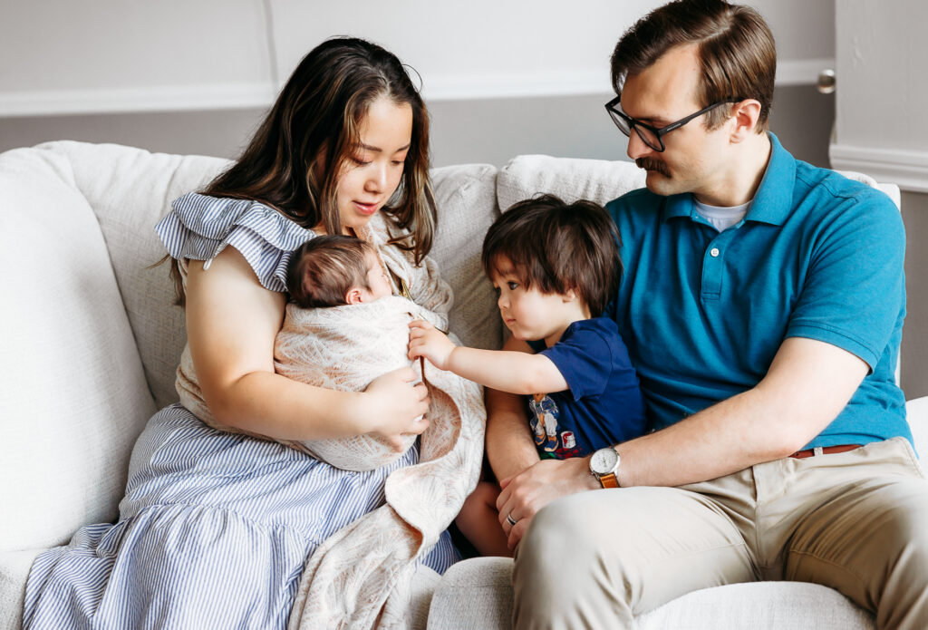 Family of four sits on couch during newborn photo session.