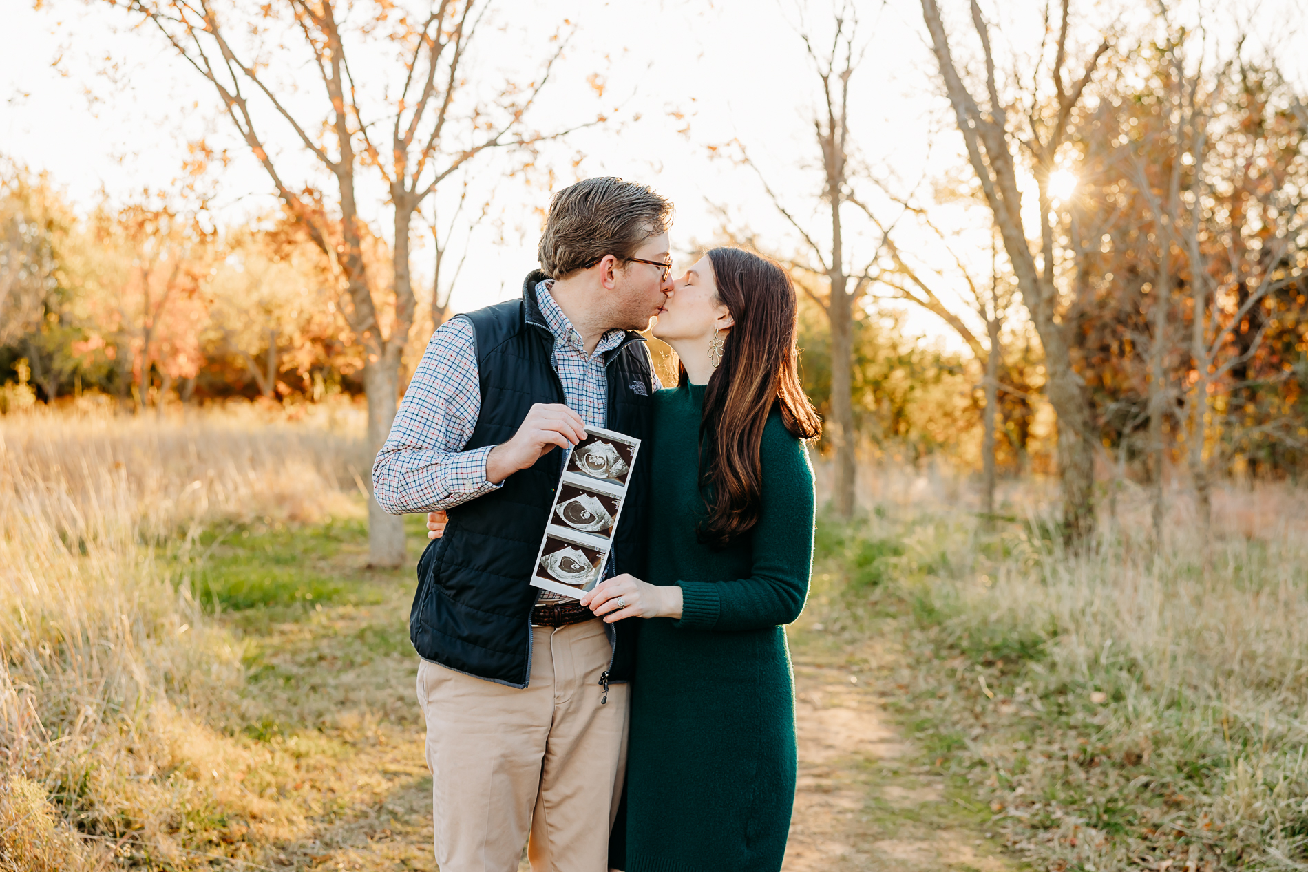 Husband and wife kiss with picture of sonogram during pregnancy announcement photo session in Edmond, OK