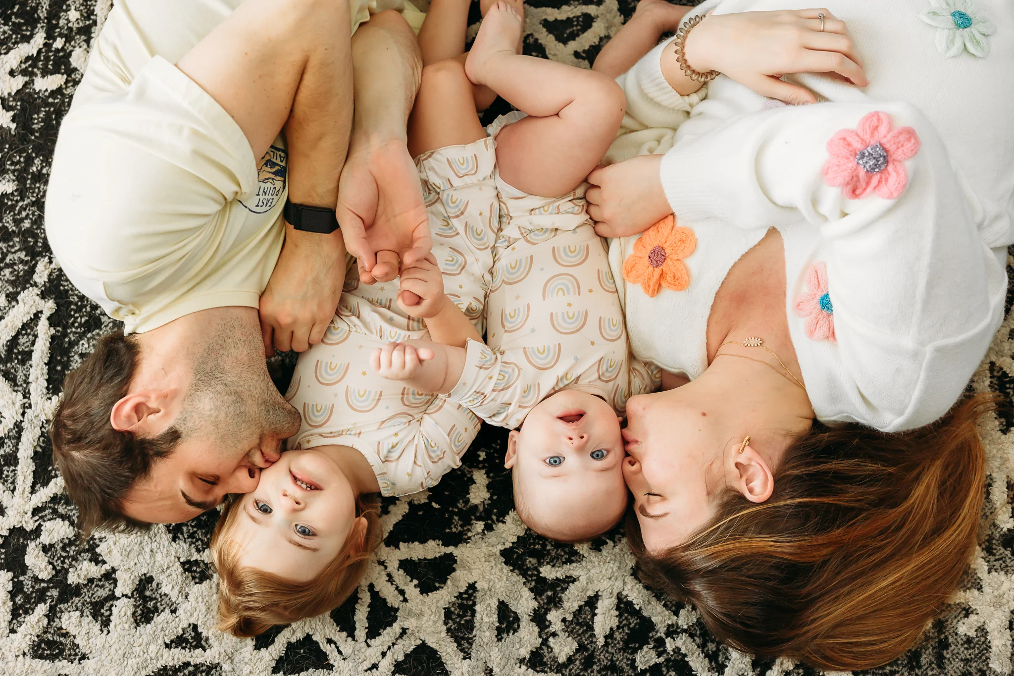 Mom and Dad kiss their toddler daughters on the living room floor during at home family photo session in OKC.