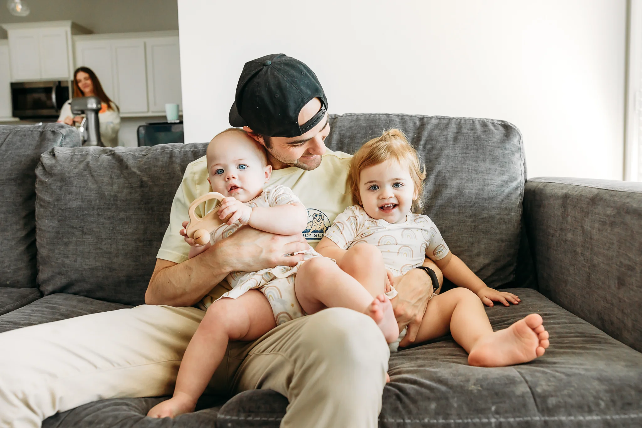 Mom and Dad kiss their toddler daughters on the living room floor during at home family photo session in OKC.