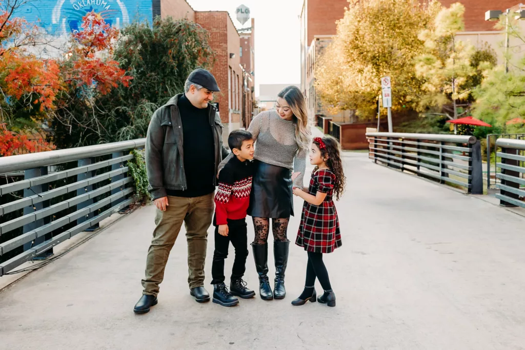 Family stands on bridge over river canal during family photography session in Bricktown, OKC.
