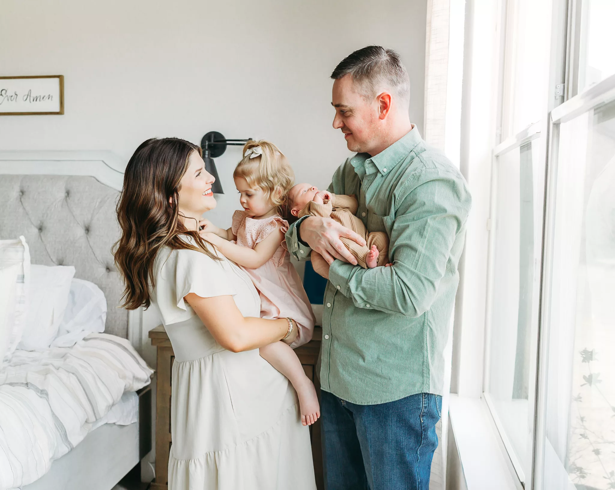A family of four stands together in bedroom during OKC newborn photography session.
