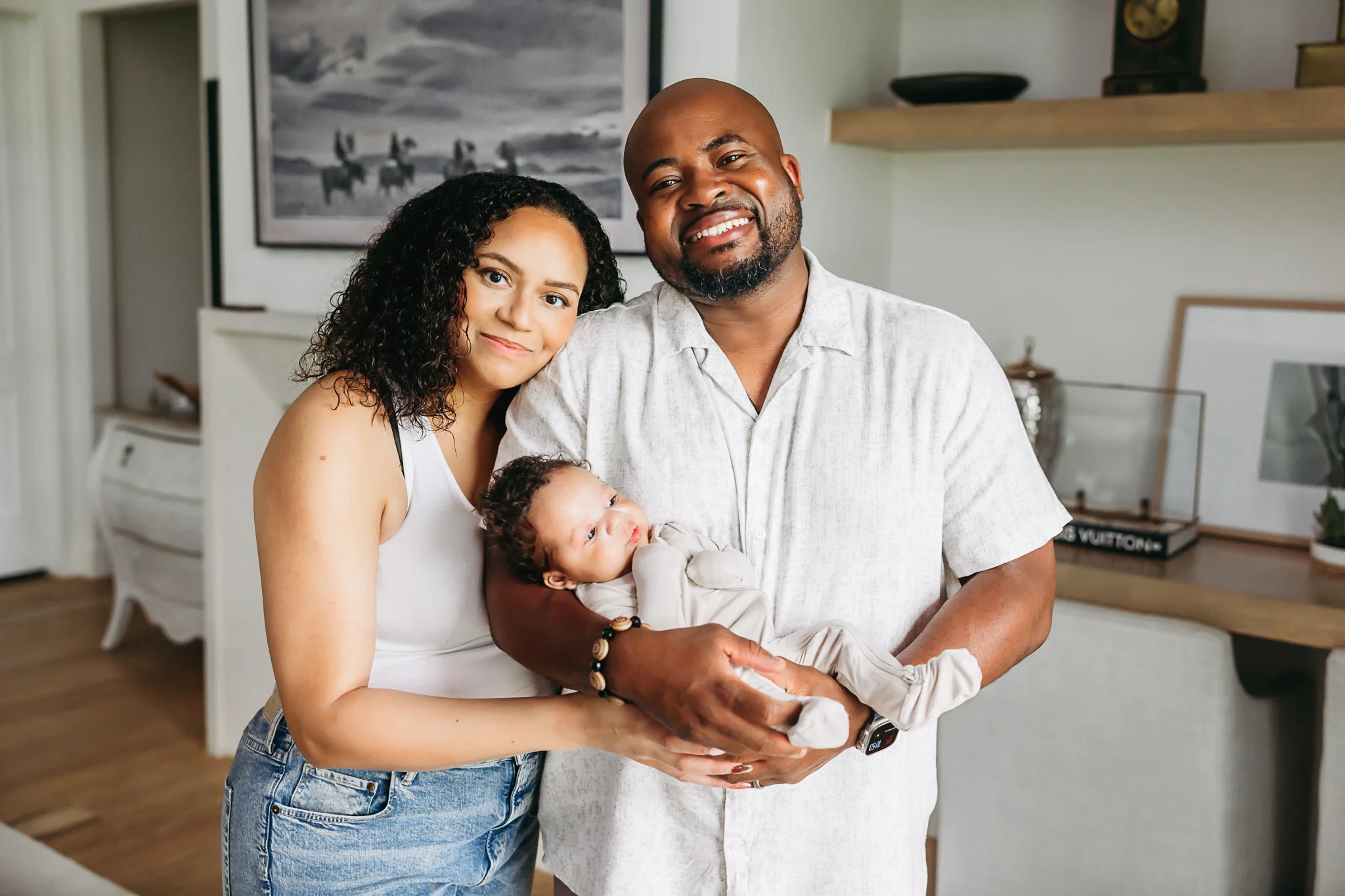 Mom and Dad in white clothes stand in living room with newborn in OKC.