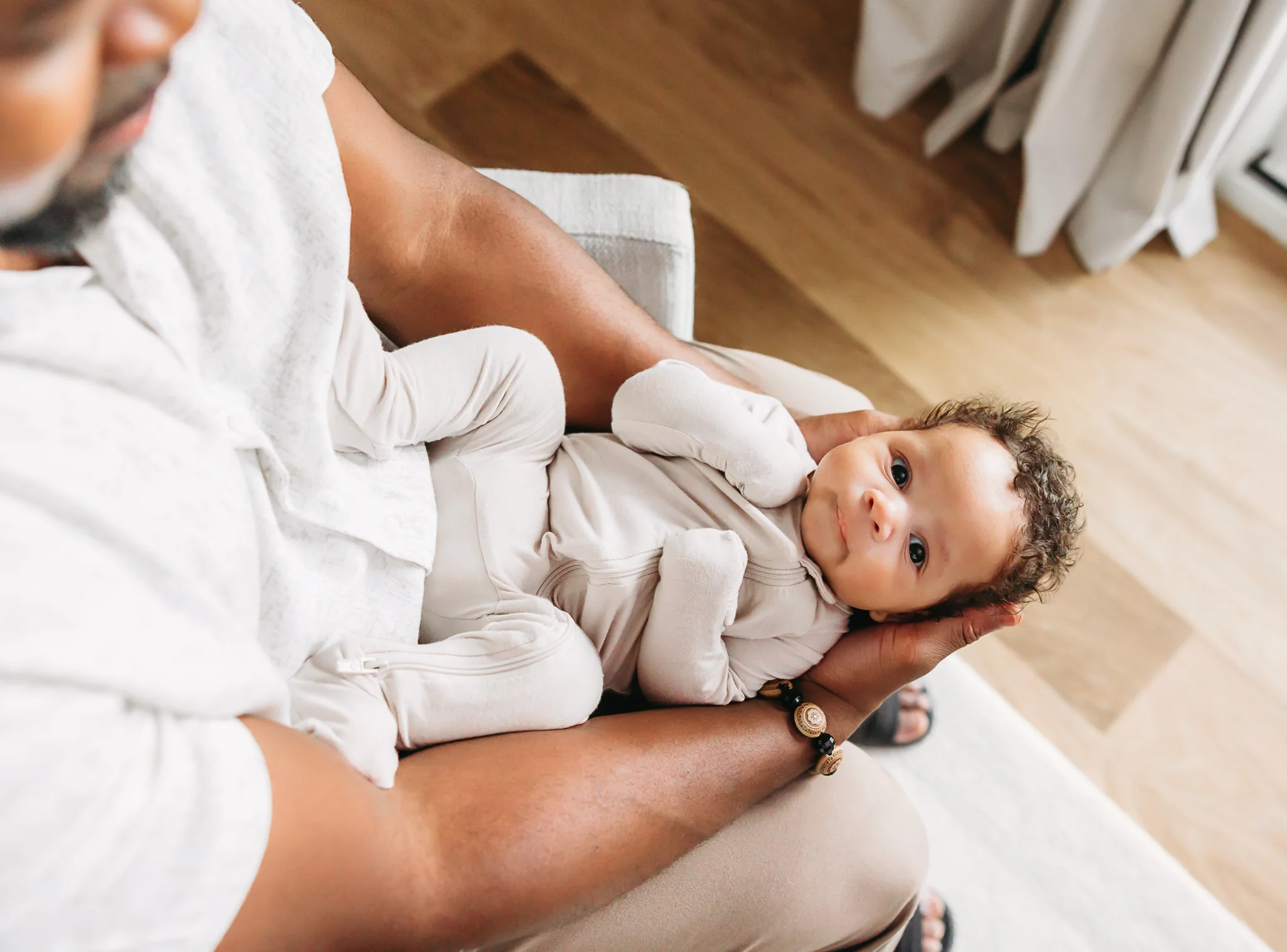 Baby in brown sleeper lays in Daddy's arms during newborn photo session.