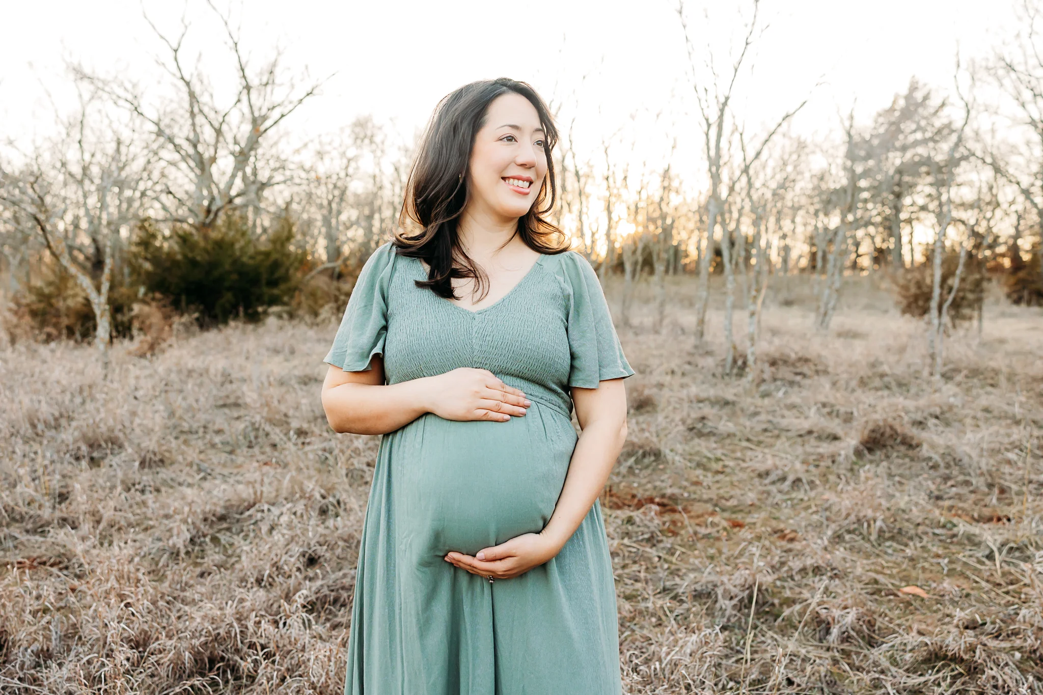 Pregnant Mom holds belly in field during a golden hour photo session at OKC Bluff Creek Park.