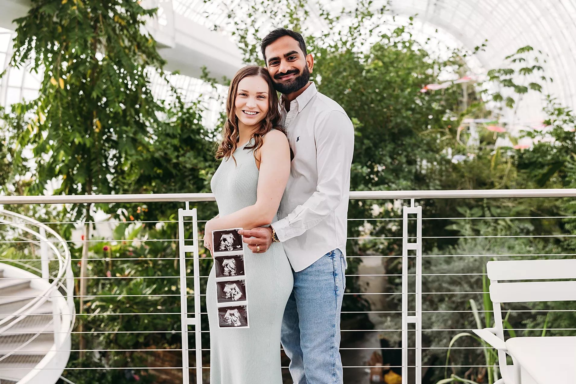 Mom and Dad in white shirts snuggle their newborn in a pink outfit.