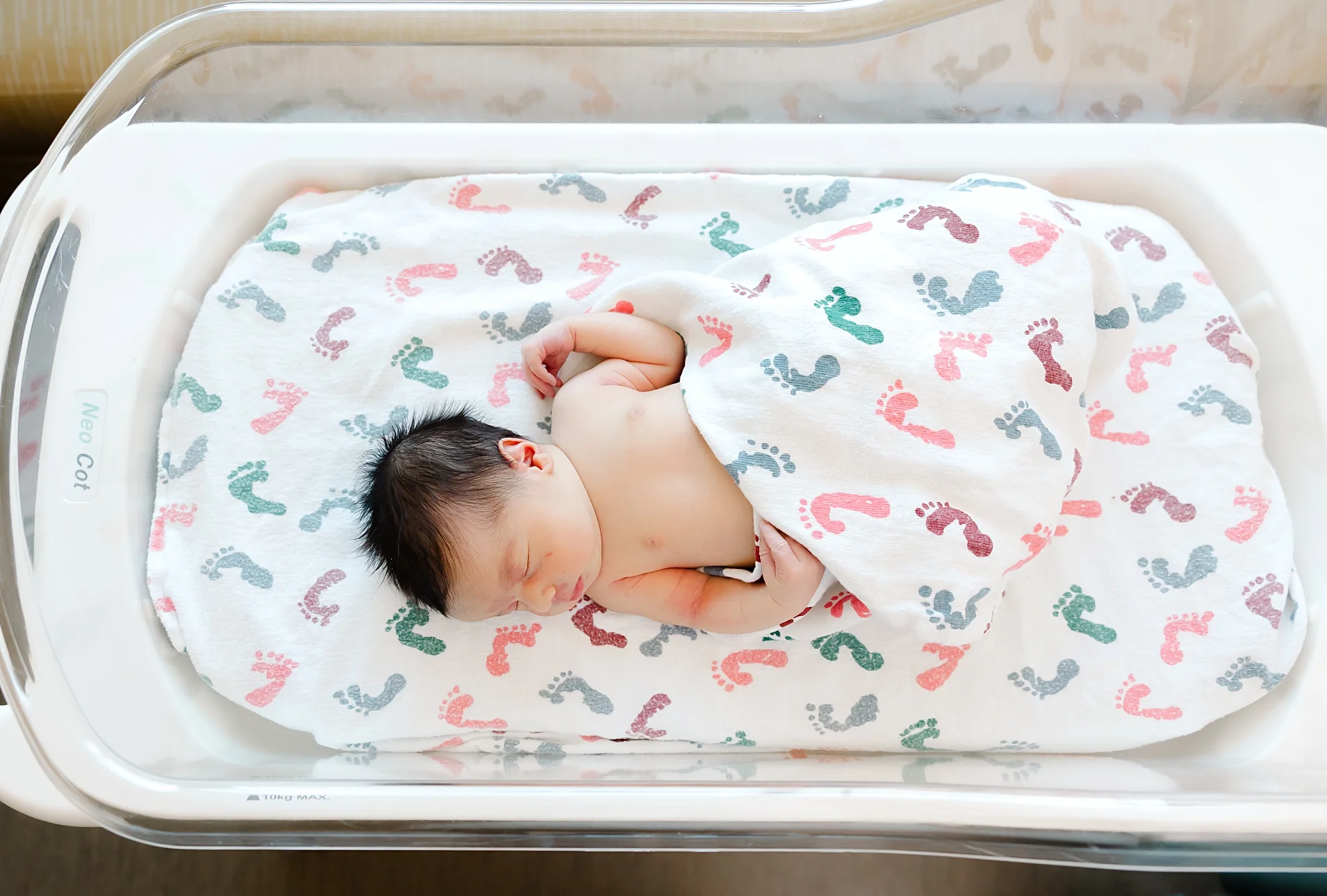 Baby lies in hospital crib in OKC hospital with hospital blanket.