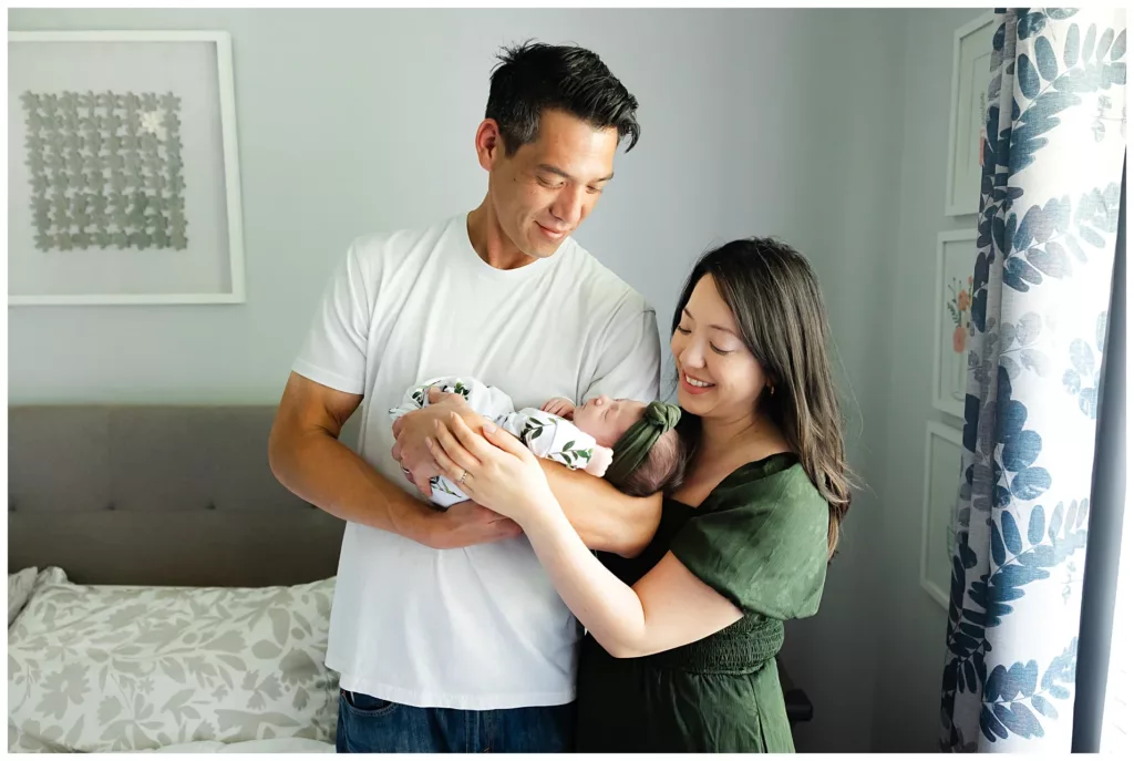 new parents stand with newborn girl during OKC lifestyle newborn sesssion.