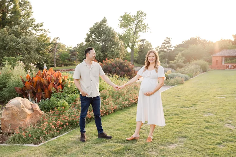A expecting couple stands in golden sunlight in the spring flowers at Will Rogers Botanical Gardens.