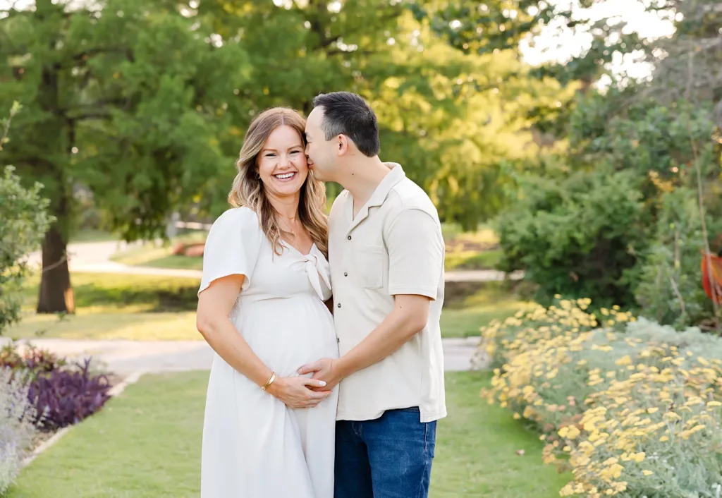 An pregnant mom stands with her husband with yellow flowers behind for Will Rogers Maternity Photos.
