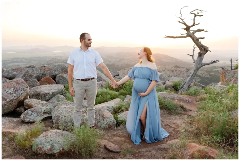 a pregnant mom in a blue dress with husband on the top of Mount Scott during golden hour for an Oklahoma maternity photo session.