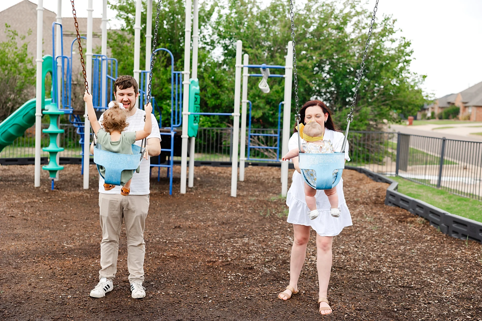 Mom, Dad and toddlers play on playground during family photos.