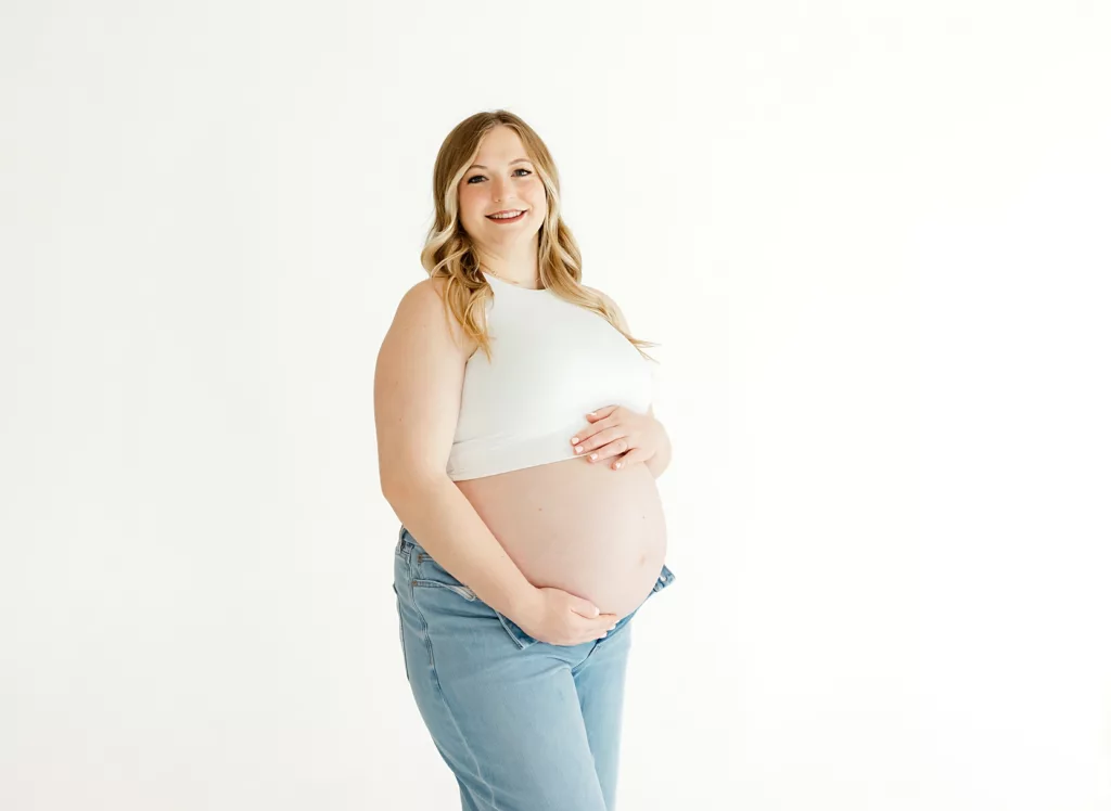 Expecting mom in jeans and white top against a white studio backdrop