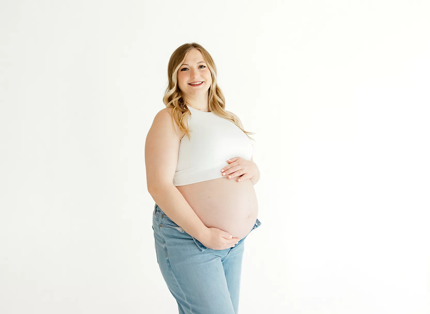Expecting mom in jeans and white top against a white studio backdrop

