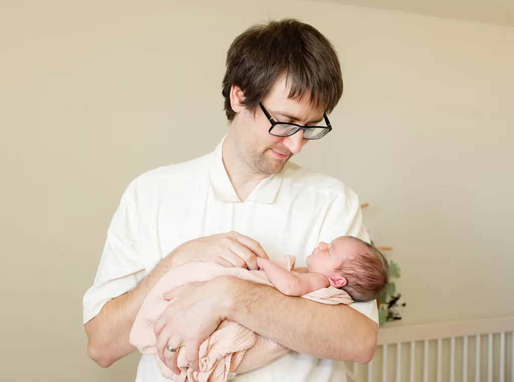 dad holds baby girl in his arms during an oklahoma city newborn photo session.