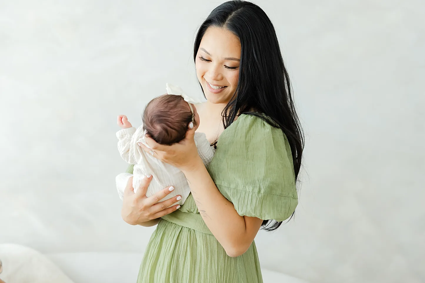A new mama in green dress smiles down at her newborn.
