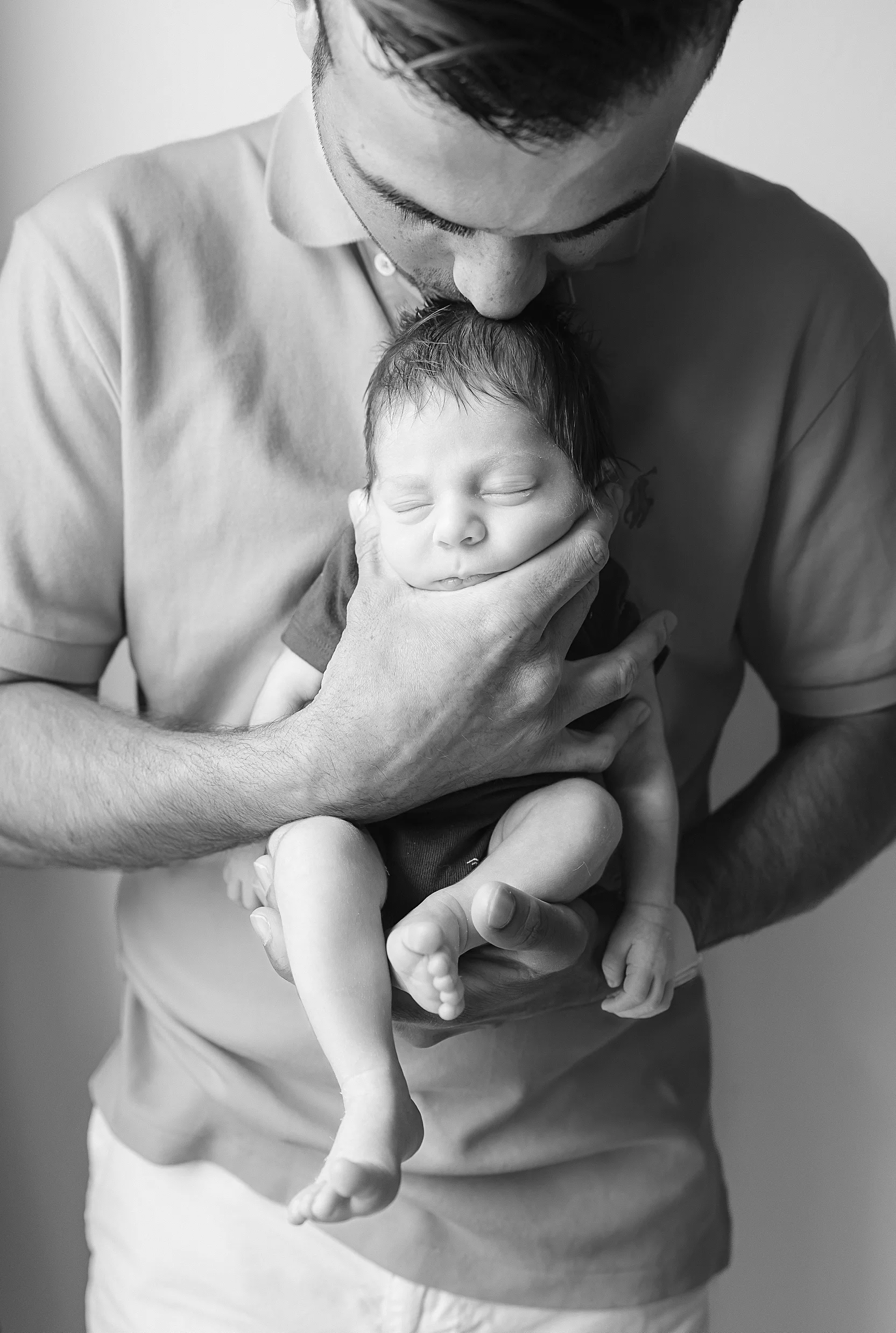 black and white image of dad kisseing his newborn son during a newborn photo session at home in OKC.